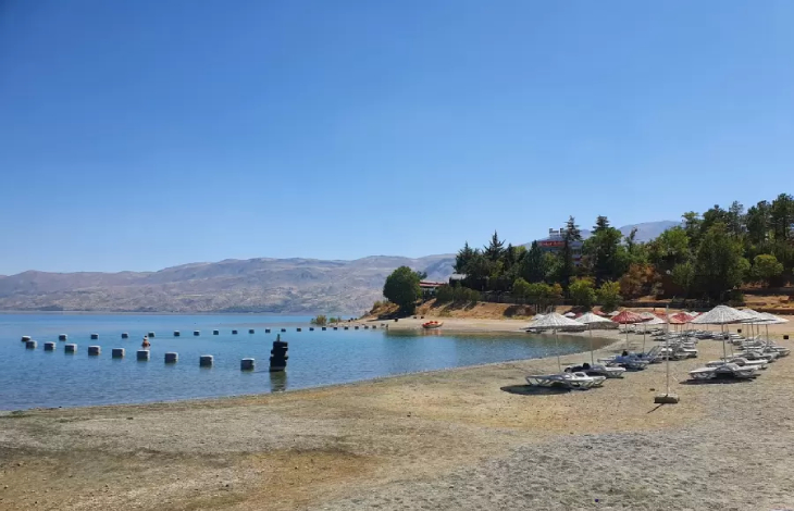 Hazar Gölü kıyısındaki kamp alanında şezlong ve güneş şemsiyelikleri bulunuyor.