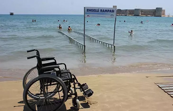 ChatGPT: Bu fotoğrafta, sahilde yer alan bir “Engelli Rampası” görülüyor. Rampa, tekerlekli sandalye kullanan bireylerin doğrudan denize girebilmesi için tasarlanmış ve denizin içine doğru uzanıyor. Ön planda boş bir tekerlekli sandalye kumsalda duruyor