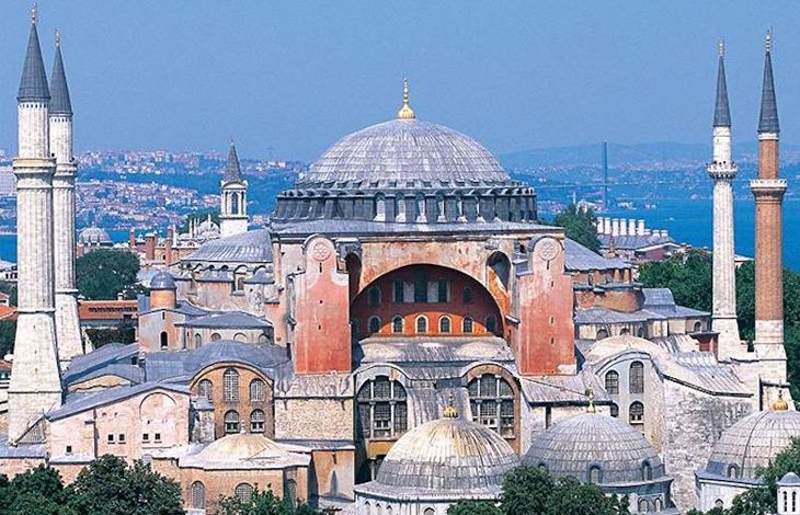 Bu fotoğrafta İstanbul'da bulunan Ayasofya Camii görülmektedir. Yapı, büyük kubbesi, kemerleri ve dört minaresiyle dikkat çekmektedir. Tarihi boyunca hem kilise, hem cami, hem de müze olarak hizmet vermiş olan Ayasofya, Bizans ve Osmanlı mimarisinin izlerini bir arada taşır. Fotoğrafta, yapının görkemli merkezi kubbesi ortada yer almakta; çevresinde ise daha küçük kubbeler ve çeşitli mimari detaylar bulunmaktadır. Arka planda Boğaz ve şehir manzarası görünmekte.