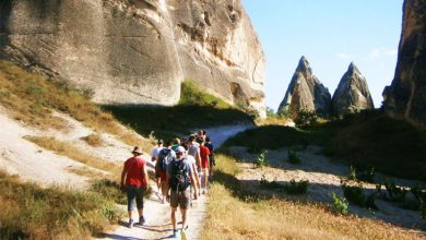 ChatGPT: Bu fotoğrafta, doğa yürüyüşü (trekking) yapan bir grup insan, Kapadokya bölgesine özgü peribacalarının arasında yürüyüş yaparken görülüyor. Katılımcılar sırt çantaları ve şapkalarıyla donanmış, patika bir yolda sırayla ilerliyorlar. Etrafta yüksek kaya oluşumları ve sarı-yeşil tonlarda doğal bitki örtüsü göze çarpıyor
