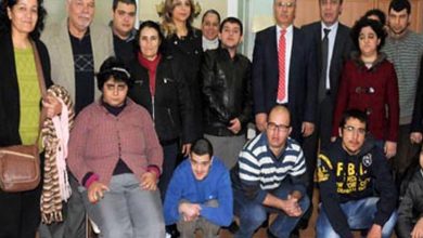 Bu fotoğraf, özel gereksinimli bireylerle birlikte çekilmiş bir toplu anı fotoğrafını göstermektedir. Fotoğrafta hem gençler hem de yetişkinler bulunuyor. Bazı bireylerin otizmli ya da zihinsel engelli bireyler olduğu gözlemlenebiliyor. Arkada takım elbiseli yetkililer ve öğretmen/veli gibi görünen bireyler yer almakta. Fotoğraf, bir ziyaret, etkinlik ya da farkındalık günü kapsamında çekilmiş olabilir. Ortam samimi ve destekleyici bir izlenim veriyor.