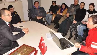 Bu fotoğraf, bir topluluk toplantısını veya kamuya açık bir görüşmeyi yansıtıyor. Masanın bir tarafında resmi kıyafetli bir yetkili otururken, diğer tarafında engelli bireyler ve destekçileri bulunuyor. Katılımcıların çoğu ciddi bir şekilde dinliyor veya konuşuyor. Masadaki Türk bayrağı ve dizüstü bilgisayar, toplantının resmi bir bağlamda gerçekleştiğini gösteriyor.