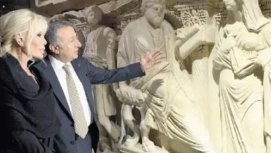 Bu fotoğraf, bir müze veya tarihi eser sergisinde çekilmiş görünüyor. İki kişi — bir kadın ve bir erkek — detaylı oymalarla süslenmiş büyük bir antik kabartmayı (muhtemelen bir lahit ya da rölyef) inceliyor. Erkek kişi eseri eliyle işaret ederek bir şeyler anlatıyor; kadın ise dikkatle dinliyor ve izliyor. Arka planda, klasik döneme ait insan figürleri ve süslemeler yer almakta. Görsel, tarihi ve kültürel mirasa duyulan ilgiyi yansıtıyor.