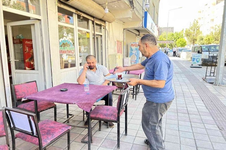 Nizam Titiz, masada telefonla görüşen bir müşterisine çay servisi yapıyor.