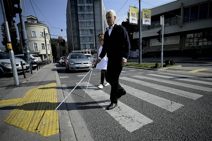 İki görme engelli birey ışıklar sayesinde duran trafikte, yaya çizgisi üzerinden beyaz bastonla yolun karşısına geçiyor.