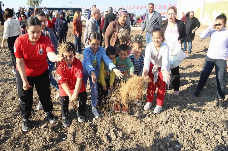 Tarlaya buğday tohumu döken çok sayıda çocuk objektife yansıyor.