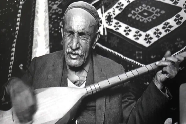 Siyah beyaz fotoğrafta Aşık Veysel bağlama çalıyor.