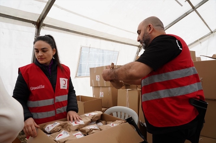 Kolilerde bulunan paket ürünlerle ilgilenen 2 Kızılay Gönüllüsü birey, objektife yansıyor.