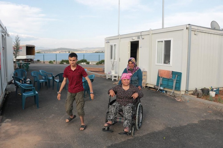 Tekerlekli sandalye ile engelli kadını taşıyan Meryem Gönen objektife yansıyor.