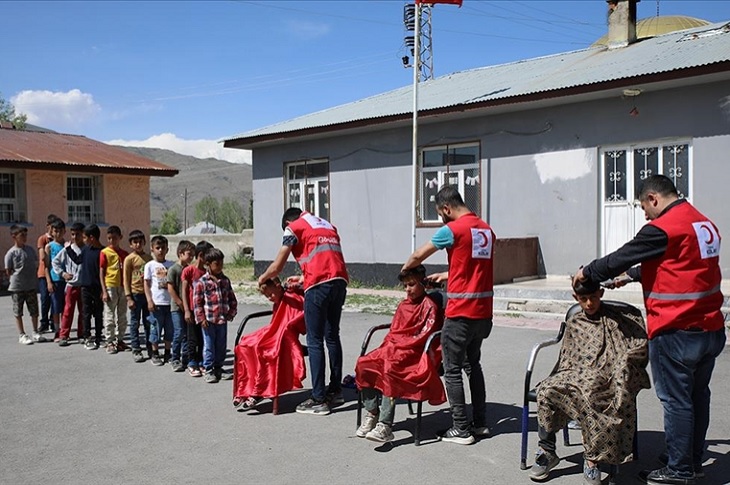 Açıkhavada tıraş edilen 3 çocuk ve tıraş sırasını bekleyen çocuklar objektife yansıyor.