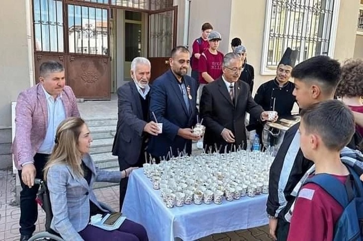 Okul bahçesinde kurulan stanttan öğrencilere aşure dağıtan gönüllüler objektife yansıyor.