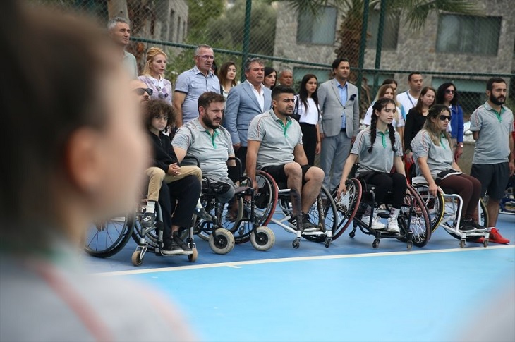 Saha kenarındaki bir grup engelli ve tekerlekli sandalyeli sporcu objektife yansıyor.