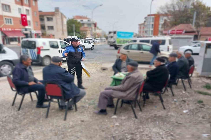 Açıkhava alanda, yaşlı bireyleri bilgilendiren bir polis memuru objektife yansıyor.