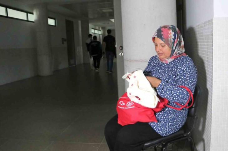 Anne Elif Doğan, üniversite koridorunda oturarak el işi yapıyor.