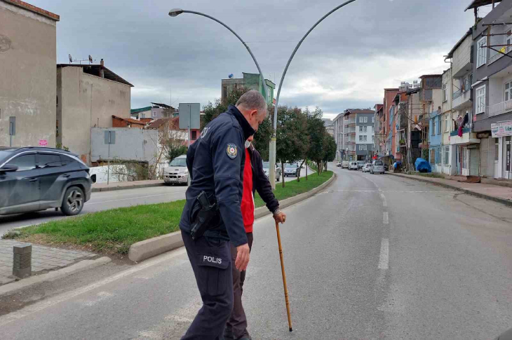 Bastonla yürüyen yayanın koluna girerek yardım eden polis memuru.