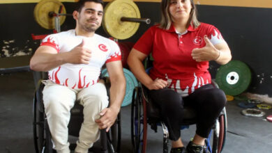 Tekerlekli sandalye üzerinde yan yana durarak fotoğraf için poz veren engelli sporcular var.