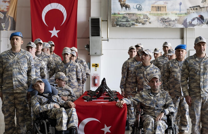 Türk bayrağı ve silahların üzerine ellerini katarak askeri yemin eden engelli bireyler var.