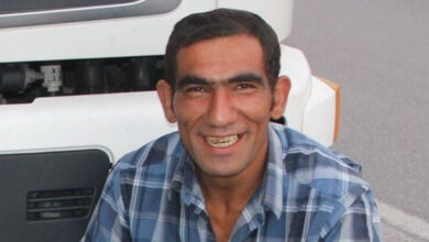 Beytullah Atılkan yerde dizlerinin üzerinde çömelerek ve bir yere yaslanarak duruyor.