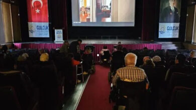 Bir sinema salonunda tekerlekli sandalye kullanıcısı engelli bireyler ve sinema koltuklarında oturan insanlar film izliyor.