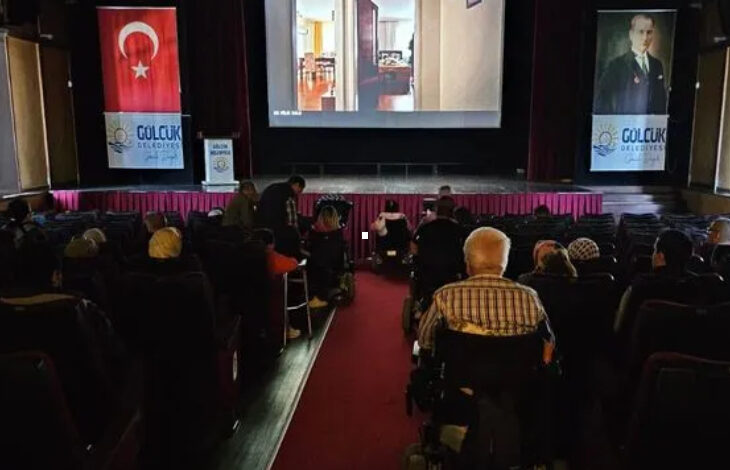 Bir sinema salonunda tekerlekli sandalye kullanıcısı engelli bireyler ve sinema koltuklarında oturan insanlar film izliyor.