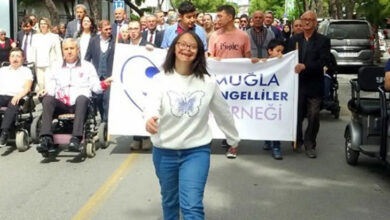 Down Sendomu olan bir birey önde, tekerlekli sandalye kullanıcıları ve pankart ile yürüyüş yapıyorlar.
