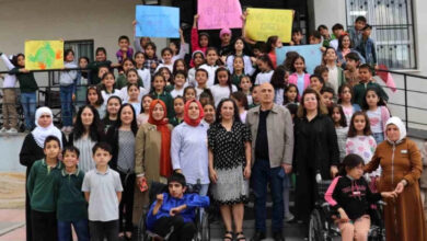 İlkokul öğrencileri, öğretmenler ve tekerlekli sandalye kullanıcısı iki çocuk fotoğraf çekiliyor.