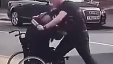 Sokak ortasında bir polis, tekerlekli sandalye kullanan adama fiziksel olarak sert bir mücadelede bulunuyor.