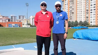 Milli Atlet Oğuz Akbulut ve antrenörü ayakta yan yana durmaktadır.