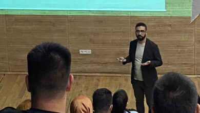 Öğr. Gör. Dr. Abdulkadir Karabulut, projeksiyon tahtasına sırtı dönük ve öğrencilerine dönük bir şekilde, ayakta konuşma yapıyor.