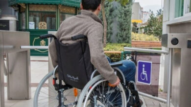 Tekerlekli sandalye kullanıcısı engelli birey, engelli giriş kapısından geçiyor.