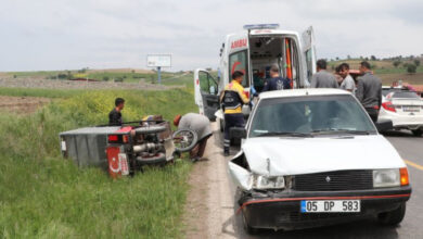 Trafik kazası olay yerinde, görsele göre sola doğru yatmış üç tekerlekli motosiklet ve beyaz bir araç var. Ambulansa yaralı taşınıyor.