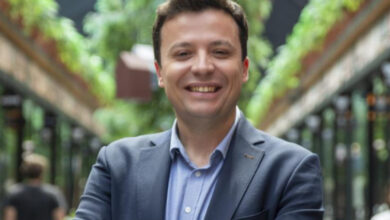 Fotoğrafta bir erkek gülümseyerek ve ayakta durarak poz veriyor.