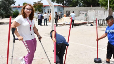 Koltuk değnekleriyle ayakta duran engelli öğretmen ve çocukların boyuna yakın ince direkleri öğrenciler belirli bir sırayla diziyorlar.