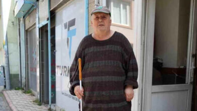 Görme engelli adam, elinde beyaz bastonu ile ayakta duruyor.