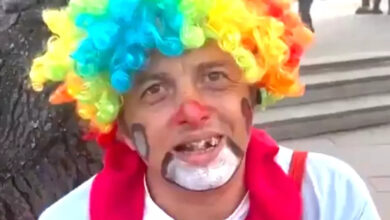 Renkli bir peruk takıp, yüzünü boyayan engelli birey kameraya gülümsüyor.