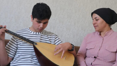 Görme engelli Umut Geçili oturduğu yerden bağlama çalıyor. Annesi de yanında oturarak dinliyor.