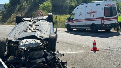 Trafik kazası sonucu ters dönmüş bir otomobil ve ambulans görselde var.