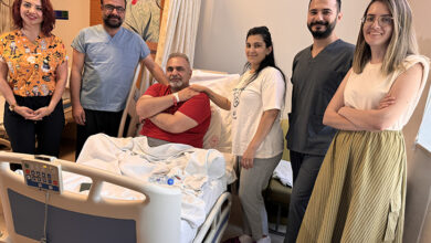 Felçli hasta ve tedavi eden doktorlar hastane odasında birlikte fotoğraf çekiliyor ve kameraya doğru bakarak gülümsüyorlar.