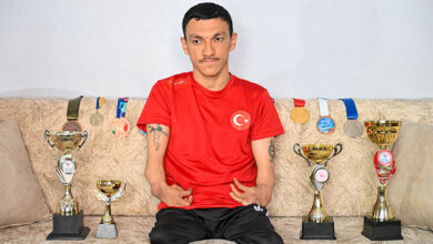 İki ayağı ampute olan engelli sporcu Umut Ünlü, bir koltuk üzerinde oturuyor iken yüzme alanında aldığı madalya ve kupaları etrafına katmış.