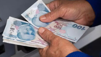 ATM önünde bir kişi elindeki 100 Türk lirası kağıt banknotları sayıyor.