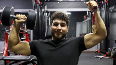 Bedensel engelli halterci Tarık Akat, bir elinde dambıl, diğerinde altın madalyasını yukarı doğru kaldırıyor.