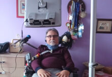 Dr Alper Kaya ALS-MNH Derneği Başkanı'trakeostomi açık şekilde önünde mikrofon başında fotoğraf çekiliyor.