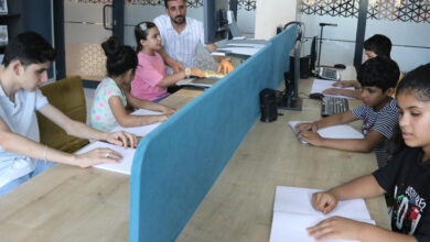 Bir masa etrafında karşılıklı oturan görme engelli çocuklar braile alfabesi ile yazılı metinleri okuyor ve bazı engelli bireylerde bilgisayar başında okuma yapıyor.