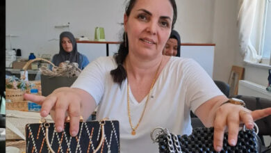 Engelli birey Dilek Çimen, çanta üzerine yaptığı takı tasarımlarını göstermek için iki çantayı, iki elinde tutarak gösteriyor.