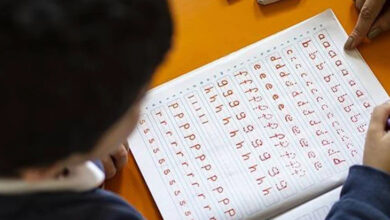 Harflerin yazılı olduğu bir defter sayfaları açık ve başında bir çocuk var.