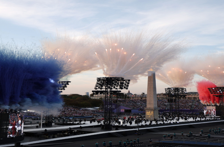 Fotoğrafta, gösteri ve konser alanının olduğu yerde beyaz, mavi ve kırmızı renklerden oluşan bir duman şeklinde gösteri yapılıyor.