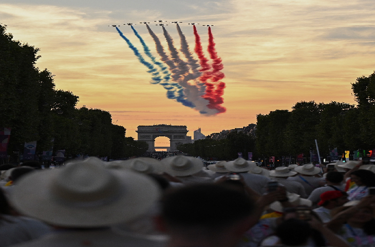 Fotoğrafta, gösteri amaçlı uçuş yapan uçakların kuyruk bölümünden bırakılan renkli boyalar Fransa bayrağını temsil ediyor. Gösteri uçuşunu izleyen kalabalık bir insan grubu uçakların altında kalıyor.