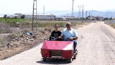 Kırmızı renkli özel tasarlanmış engelli aracında görme engelli İbrahim Merter ve bedensel engelli oğlu Mustafa Sait Merter’in yolda çekilmiş bir fotoğrafı.