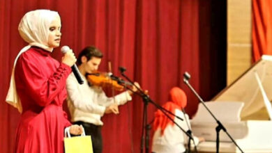 Görme engelli birey Şerife Koyuncuoğlu, sahnede elindeki mikrofon ile şarkı söylüyor. Görselde arka tarafta kalacak şekilde keman çalan birileri flu şekilde var.