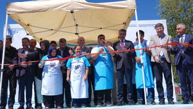 Kırmızı renkli kurdelenin arkasında otizmli ve Down sendromlu bireyler var. Engelli bireylerin arkasında protokol üyeleri, Erzurum Büyükşehir Belediye Başkanı Mehmet Sekmen ve törene diğer katılan kişiler var.